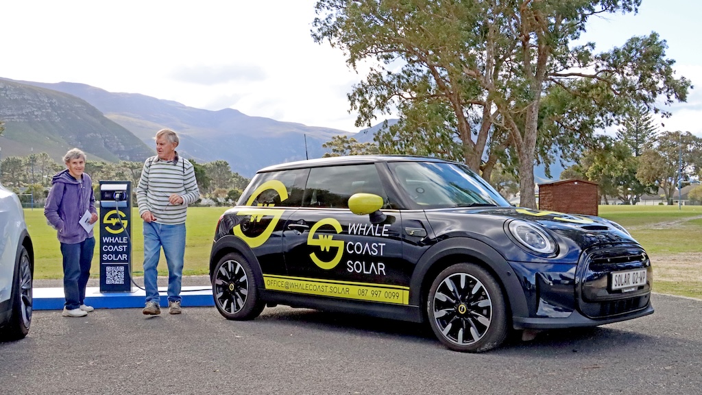 Man, woman, and MINI Cooper SE with Whale Coast Solar branding