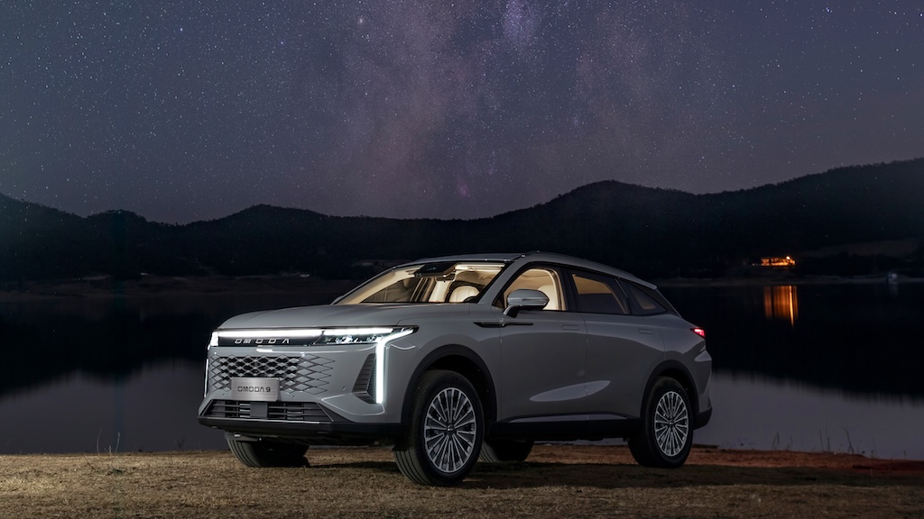 Omoda C9 PHEV at night, water and cottage in background